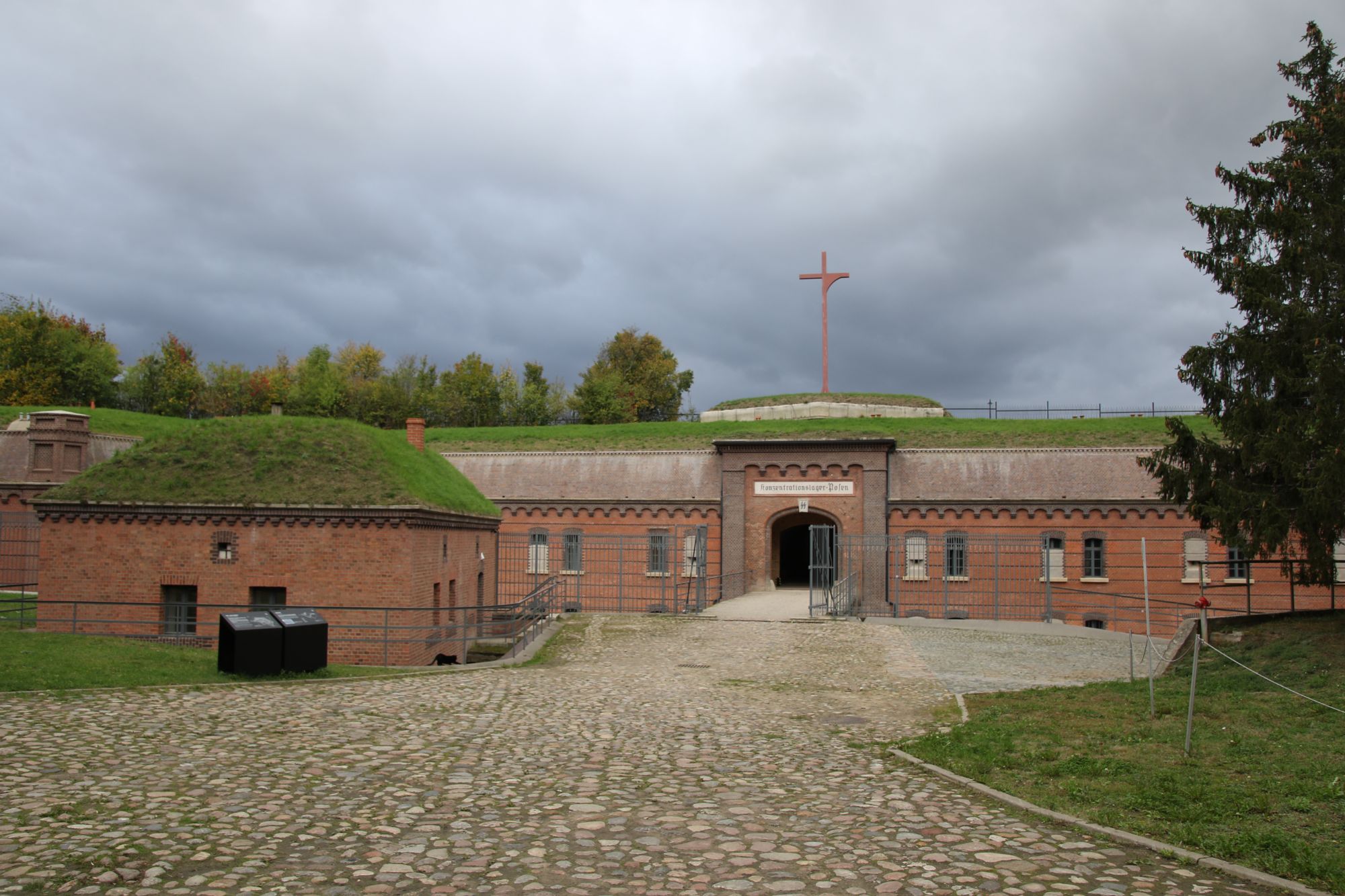 The brick entrance gate of Fort VII with its historic inscription and a cross on the earth rampart above it
